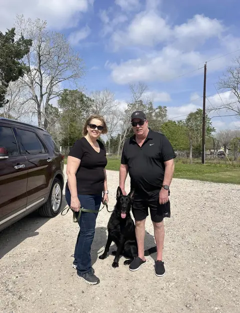 Happy clients standing with their trained black German Shepherd